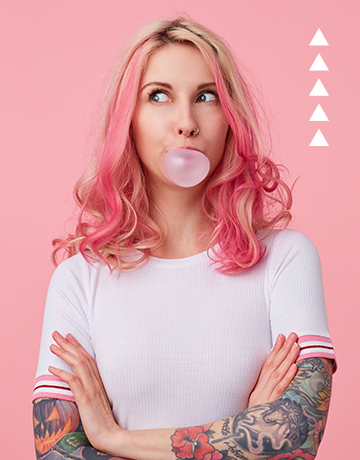 a woman with pink hair blowing a bubble.