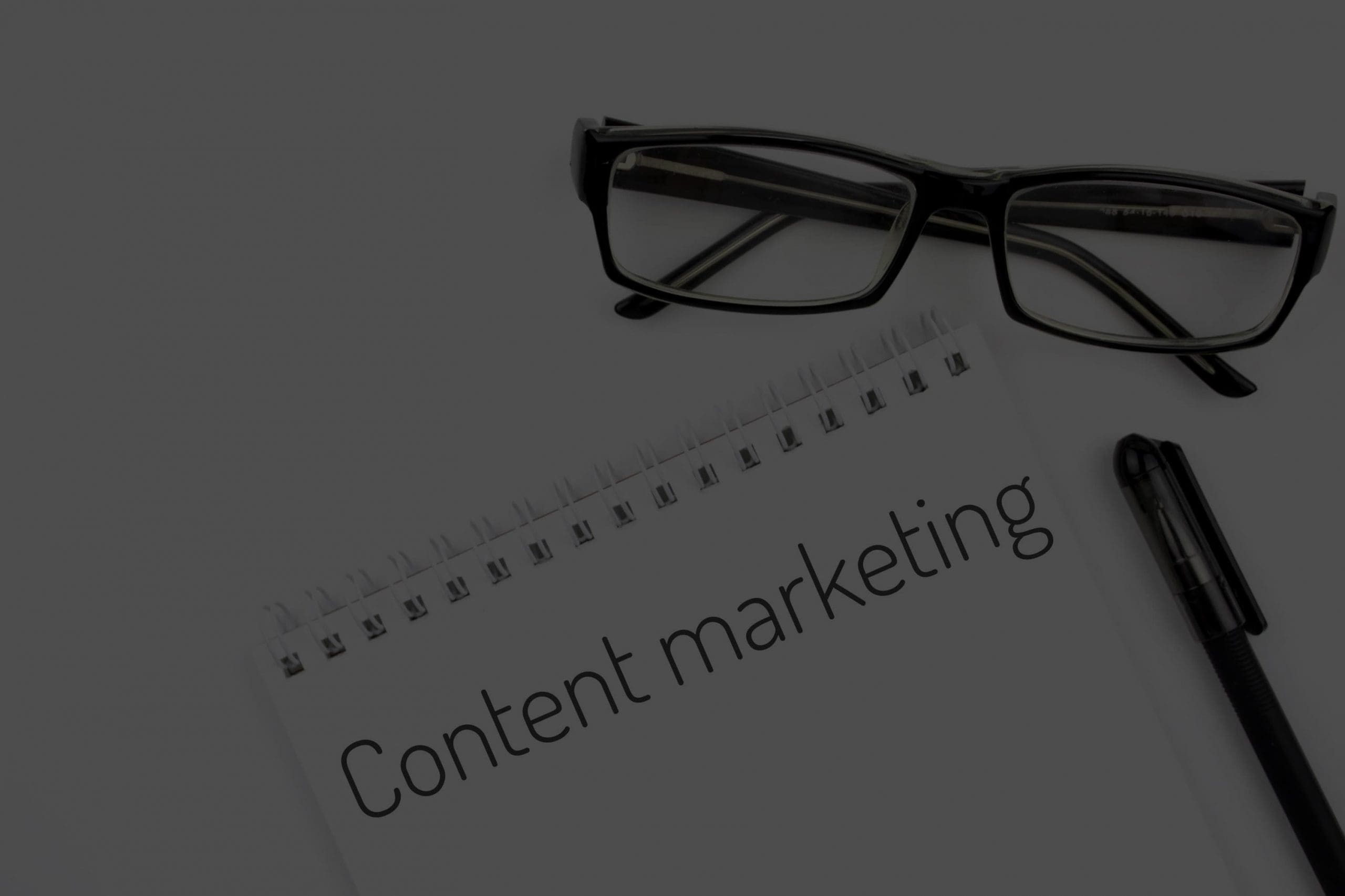 a notepad with the words content marketing on it next to a pair of glasses.